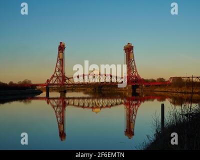 The Newport Bridge against a gradated blue and orange sky. The foreground shows the still, glassy River Tees reflecting the scene and sky. Stock Photo