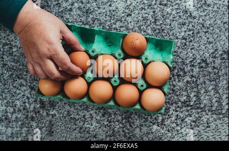 Adult woman's hand taking an egg from a green recycled paper panel on the granite counter in the kitchen. Top view