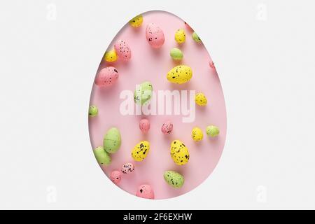 Egg shape cut in the white paper with different colorful Easter eggs. Minimal spring holidays concept. Stock Photo