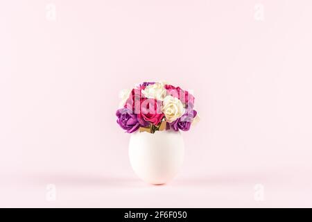 Spring flowers in cracked eggshell against pastel pink background. Easter minimal concept. Creative Happy Easter or spring layout. Stock Photo