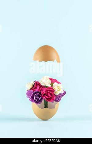 Spring flowers in cracked eggshell against pastel blue background. Easter minimal concept. Creative Happy Easter or spring layout. Stock Photo