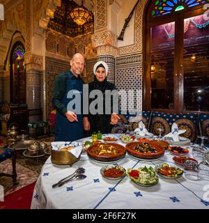 Rabia Hassan presents a richly laid table with several tagine dishes and starters at the Dar Saada restaurant in the medina of Fès, Morocco Stock Photo