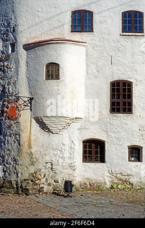 Facade of an old building with plastered white walls and arched windows with bars in the old part of the city of Vyborg. Stock Photo