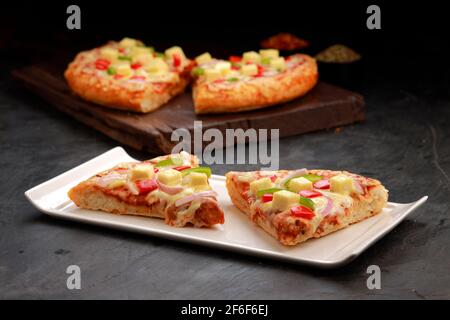 Pizza Paneer Makhani ,  made using red and green bell pepper ,onion ,paneer and mozzarella cheese,thin pastry crust slices placed on wooden board and Stock Photo