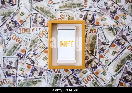 Non-fungible token NFT, crypto art, digital art, new type of cryptorurrency. Cell phone with golden NFT text in golden frame as art object on dollars Stock Photo