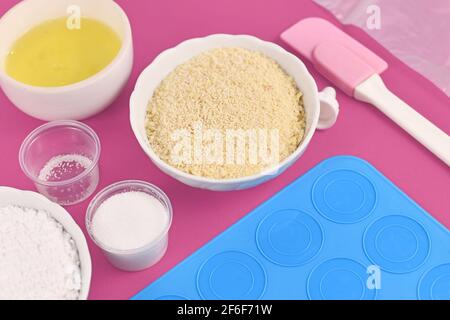 Ingredients for making homemade French Macaron sweets including powdered sugar, ground almonds, egg white, salt and mold mat on pink background Stock Photo