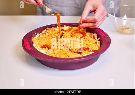 Woman puts baked bell peppers on homemade quiche pie with chicken, dried tomatoes, cheddar cheese on light background. Close up, copy space Stock Photo