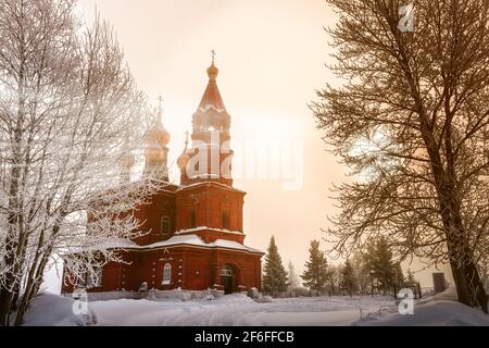 There are trees near the church at sunset. The branches of the trees are covered with thick white frost. The oak glows because the sun shines through Stock Photo