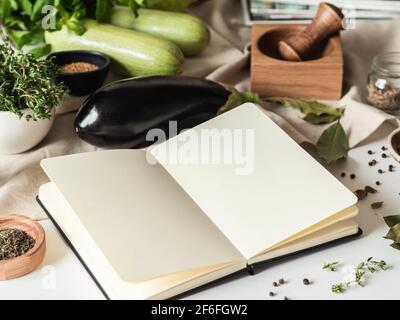 Open notebook for cooking recipes and various vegetarian ingredients on kitchen table. Front view Stock Photo