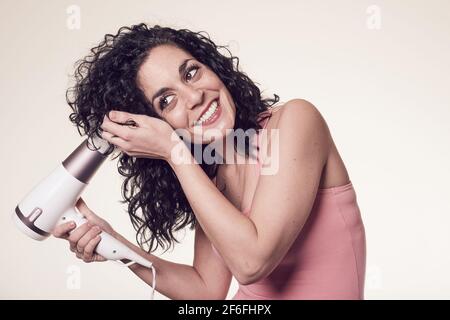 young black curly haired woman follows the curly girl method with suitable curly hair care products using a blow dryer to get curls and waves in her h Stock Photo