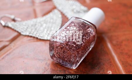 Rose gold sparkle nail polish, soft-focus, laying on terracotta tile next to a pair of sparkly diamond earrings, Ontario, Canada, 2021. Stock Photo