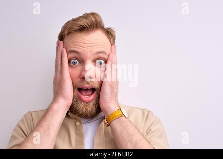 close-up portrait of shocked bearded man standing with wide opened mouth and eyes and touching face, scream. isolated white background Stock Photo