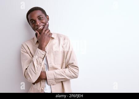 Optimistic African Male Touching Chin Thinking, Stand In Contemplation Looking At Camera, In Casual Jacket, Isolated On White Stock Photo
