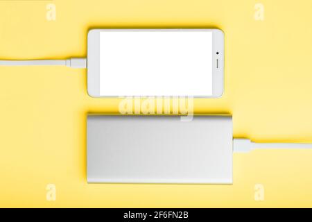 Power Bank charges your smartphone on a yellow background. Universal external battery for gadgets free space and minimalistic composition. Portable ch Stock Photo