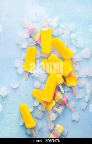 Exotic fruit ice cream sticks on blue background with ice cubes. Top view, blank space Stock Photo