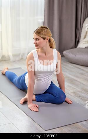 nice baby expectant sitting on mat exercising, engaged in fitness alone at home, healthy active pregnancy period, enjoy sport and yoga stretching, in Stock Photo