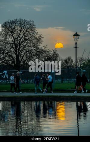London, UK. 31st Mar, 2021. The sun sets on a fine evening - People take advantage of the last day of the unseasonably warm weather and of the next stage of easing of restrictions of lockdown 3 on Clapham Common. Credit: Guy Bell/Alamy Live News