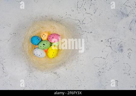 Multicolored Easter eggs in a nest on a white concrete background. Place for an inscription. View from above. Stock Photo