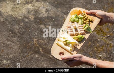 Hands holding wood platter with dairy products, nicely assorted on board. Stock Photo