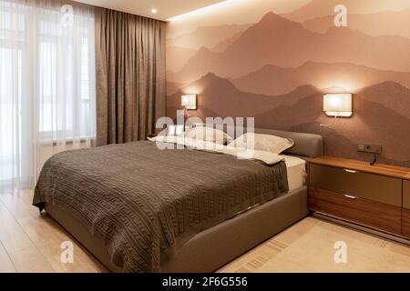 Modern bedroom in the apartment, in neutral earthy tones. Double bed with a soft textile headboard. Small photographs on the bedside table, mock-up. M Stock Photo