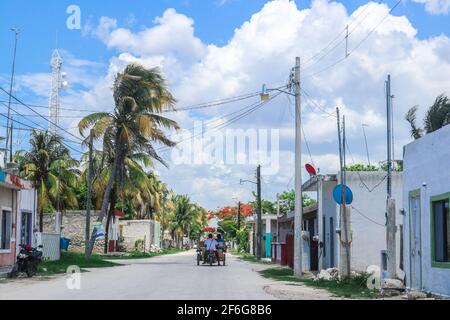 Yucatan Mexico village with motorcycles and a man transporting women in a motorcycle buggy with palm trees and lots of tangled wires and transmitter t Stock Photo