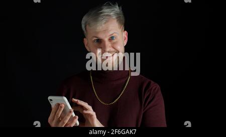 Smiling happy stylish young man using mobile phone, look surprised wow feeling happiness, enjoyment Stock Photo