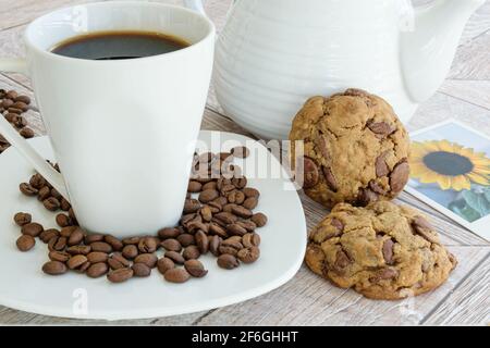 Closeup of chocolate drops cookies supported on the teapot. Next to a cup and coffee beans and a photo of sunflowers. Stock Photo