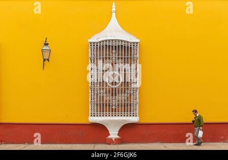 Senior peruvian man walking with blurred motion in front of a colonial style facade with window, Trujillo, Peru. Stock Photo