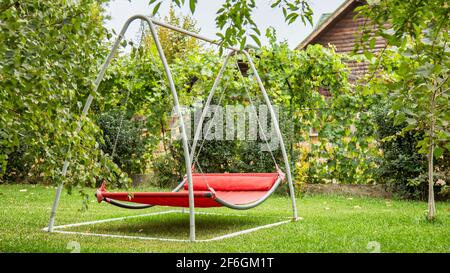 Hen geluk schouder Red hammock swing in metal frame with nobody on green lawn in backyard near  log house cottage. Rest relax relaxation alone on hammock swing in Summer  Stock Photo - Alamy