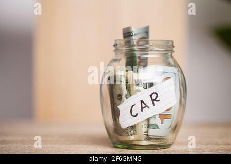 Dollar bills in glass jar and text car on wooden table
