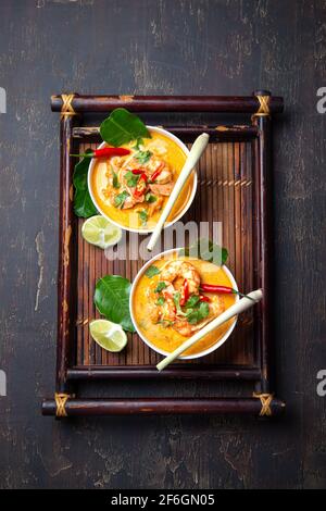 Shrimps Tom Yam Kung in white bowls on autentic thai tray top view, wooden background Stock Photo