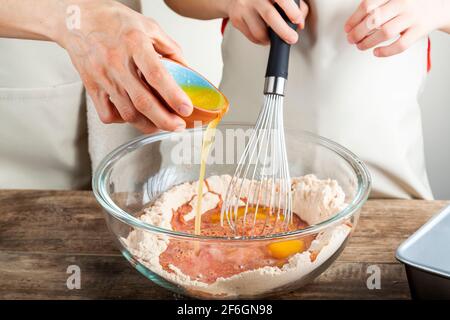 Mother and daughter cooking together in the kitchen concept with the girl holding a whisk and the woman carefully pouring melted butter or egg yolk in Stock Photo