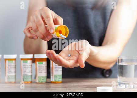a young caucasian woman is taking a pill out of the medication bottle. She has a stack of bottles lined up at the back. Concept image for drug use, ch Stock Photo