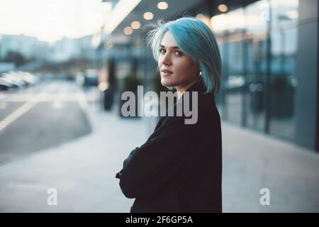 Blue haired caucasian woman is posing outside smiling at camera near a building Stock Photo