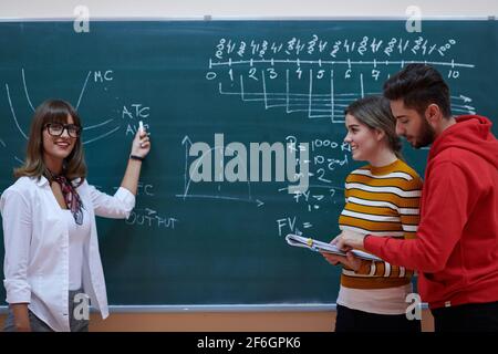 an attractive teacher with glasses explains to the students how to do the task on the board Stock Photo