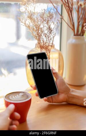 Hands of woman using mobile phone, cell phone in coffee shop. Hands of women holding blank empty screen smart phone in cafe. Women relax with mobile p Stock Photo
