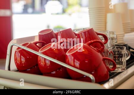 Lots of ceramic red coffee cups on espresso machine shelf in coffee shop. Selective focus. Red coffee cups on coffee machine in cafe soft focus select Stock Photo