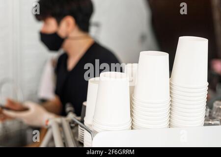 A lot of white disposable paper cups on coffee machine with cofe shop background. The stack of paper cup in the cafe. close up recycle white paper cup Stock Photo