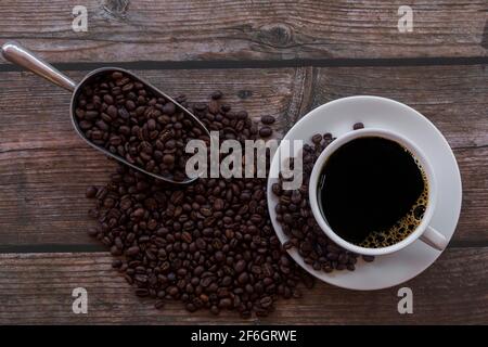 Top view cup of coffee and coffee beans in a sack on wood background. Close up hot black espresso coffee in white cup with coffee beans and sack on wo Stock Photo