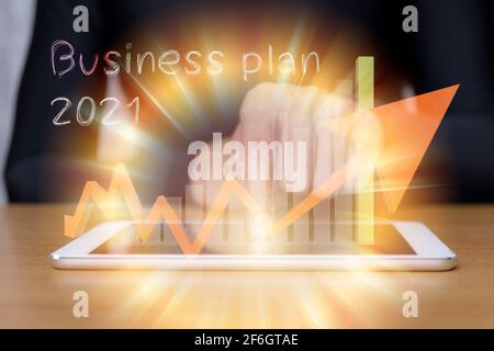 businessman hand touching on 2021 virtual screen with tablet on desk. business concept new year. Hand of businessman point to tablet with graph up and Stock Photo