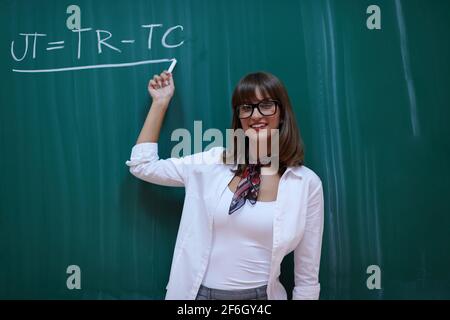 an attractive teacher with glasses explains to the students how to do the task on the board Stock Photo
