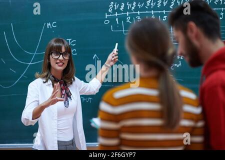 an attractive teacher with glasses explains to the students how to do the task on the board Stock Photo