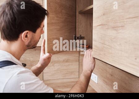 Repairman in uniform fixing cabinet at kitchen. Man open kitchen cupboard Stock Photo