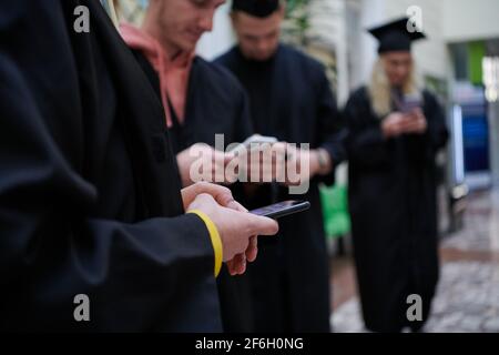 education, graduation, technology and people concept - group of happy international students in mortar boards and bachelor gowns with diplomas using m Stock Photo