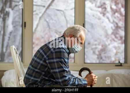 Senior man wearing protective mask sitting near window Stock Photo