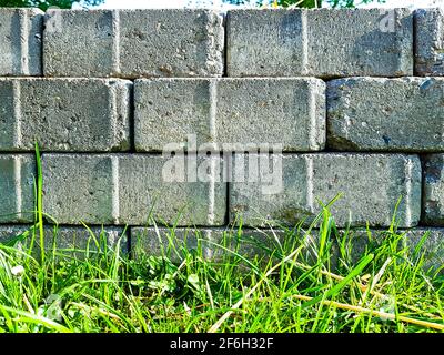 Dry stone wall bricks  pavement stones concrete gray stacked masonry boundary, fence border grass sun bed border background old architecture weathered Stock Photo