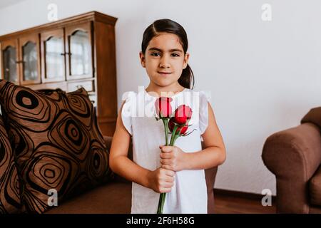 latin little girl daughter congratulates mom and gives her flowers for Happy mother's day at home in Mexico city Stock Photo