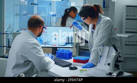 Lab technicians talking on video call with professional chemist doctor explaning vaccine reactions, woman nurse showing blood sample on web cam, during virtual meeting in medical research laboratory Stock Photo