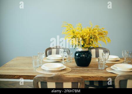 Festive Easter table setting. Branches of mimosa in vase. Home interior. Stock Photo