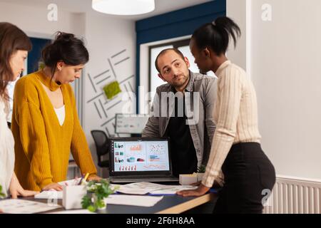 Diverse businesspeople communicating in start up business office standing over desk looking through financial documents. Multiethnic team analysing company informations in modern workplace Stock Photo